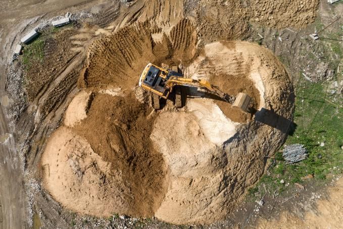 Una excavadora retira tierra en una cantera arenosa con grandes montículos de tierra.