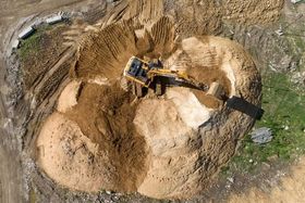 Una excavadora retira tierra en una cantera arenosa con grandes montículos de tierra.