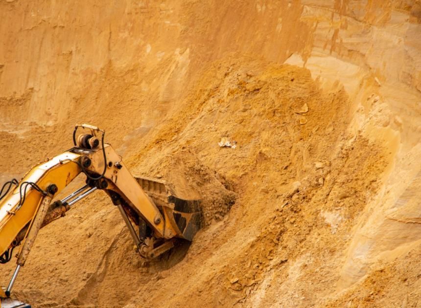 Excavadora amarilla excavando en un acantilado arenoso en una obra de construcción.
