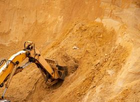 Excavadora amarilla excavando en un acantilado arenoso en una obra de construcción.