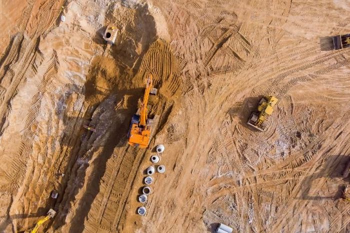 Vista aérea de una excavadora naranja y una topadora amarilla trabajando en una obra de construcción arenosa.
