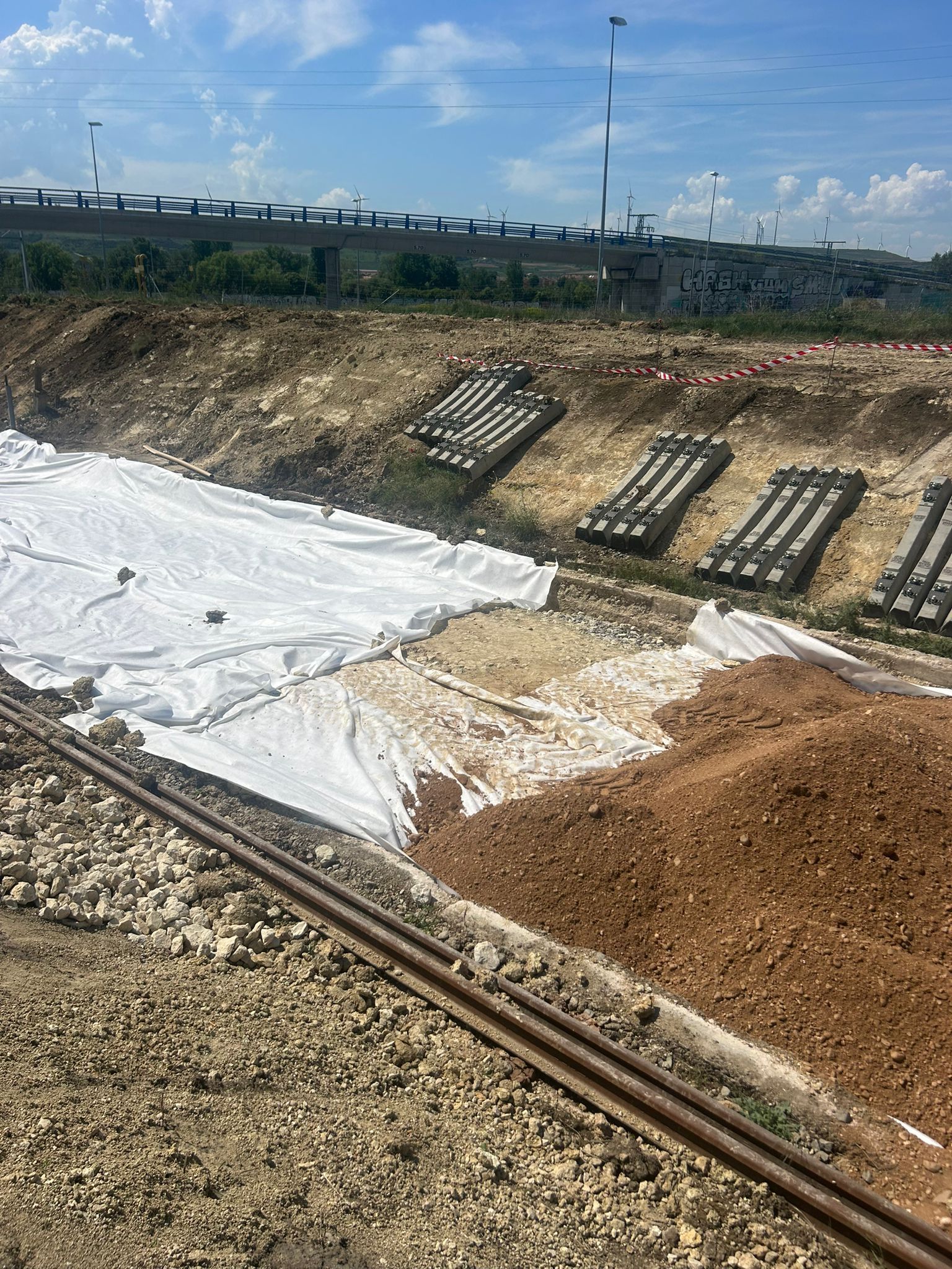 Obra en construcción con una ladera cubierta con lona blanca, montones de grava