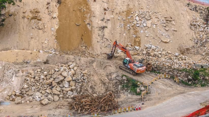 Excavadora trabajando en una obra rocosa con un terraplén empinado de tierra y grava.
