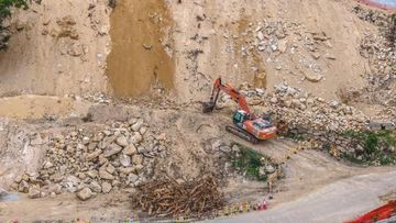 Excavadora trabajando en una obra rocosa con un terraplén empinado de tierra y grava.