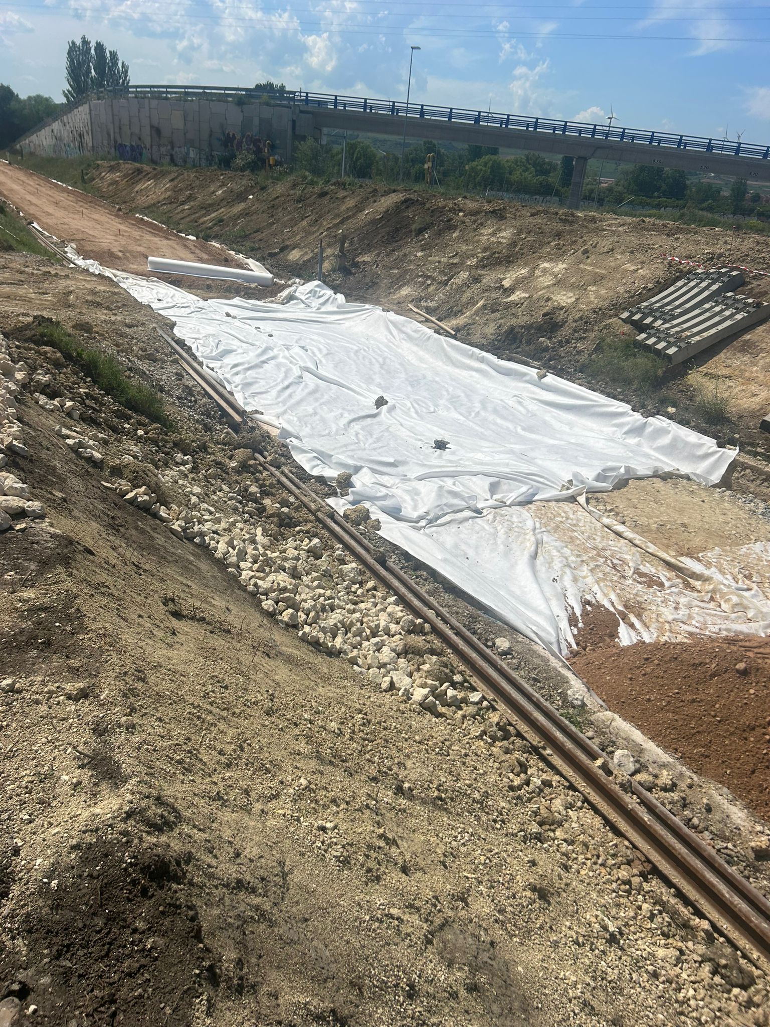 Amplio canal de drenaje seco revestido con lona blanca en un terraplén de tierra árida bajo un cielo despejado.