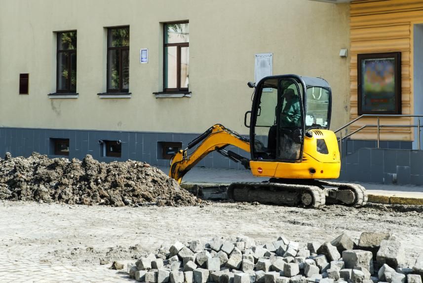 Miniexcavadora amarilla en una obra en construcción junto a un edificio y montones de escombros.