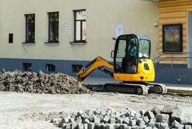 Miniexcavadora amarilla en una obra en construcción junto a un edificio y montones de escombros.