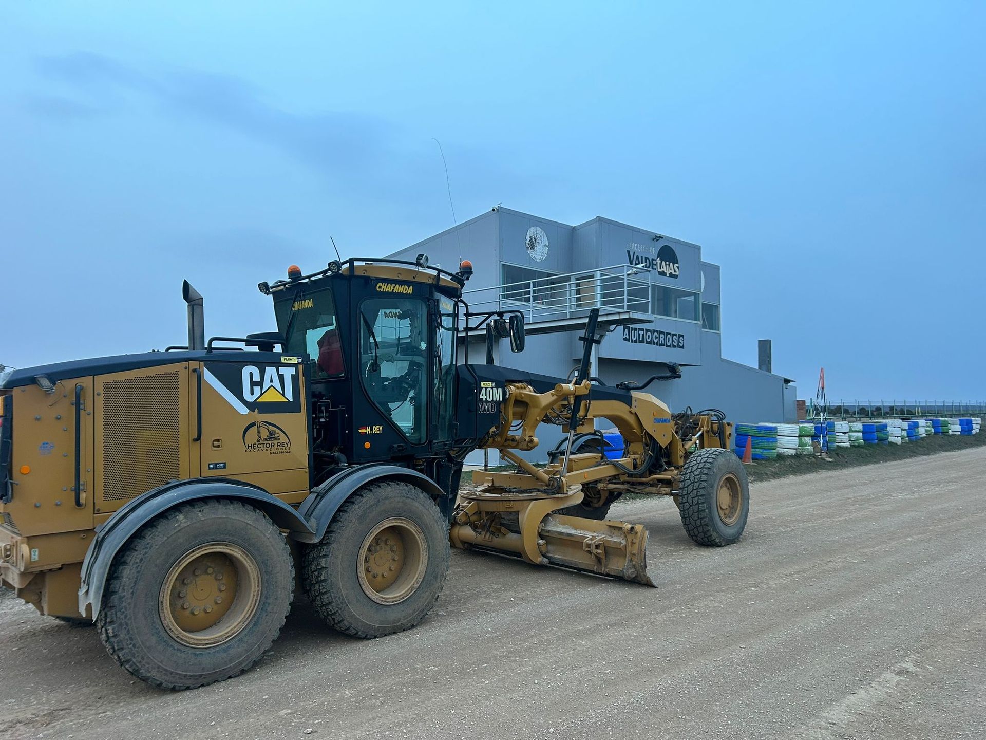 Una motoniveladora CAT amarilla y un camión volquete estacionados en un terreno de grava