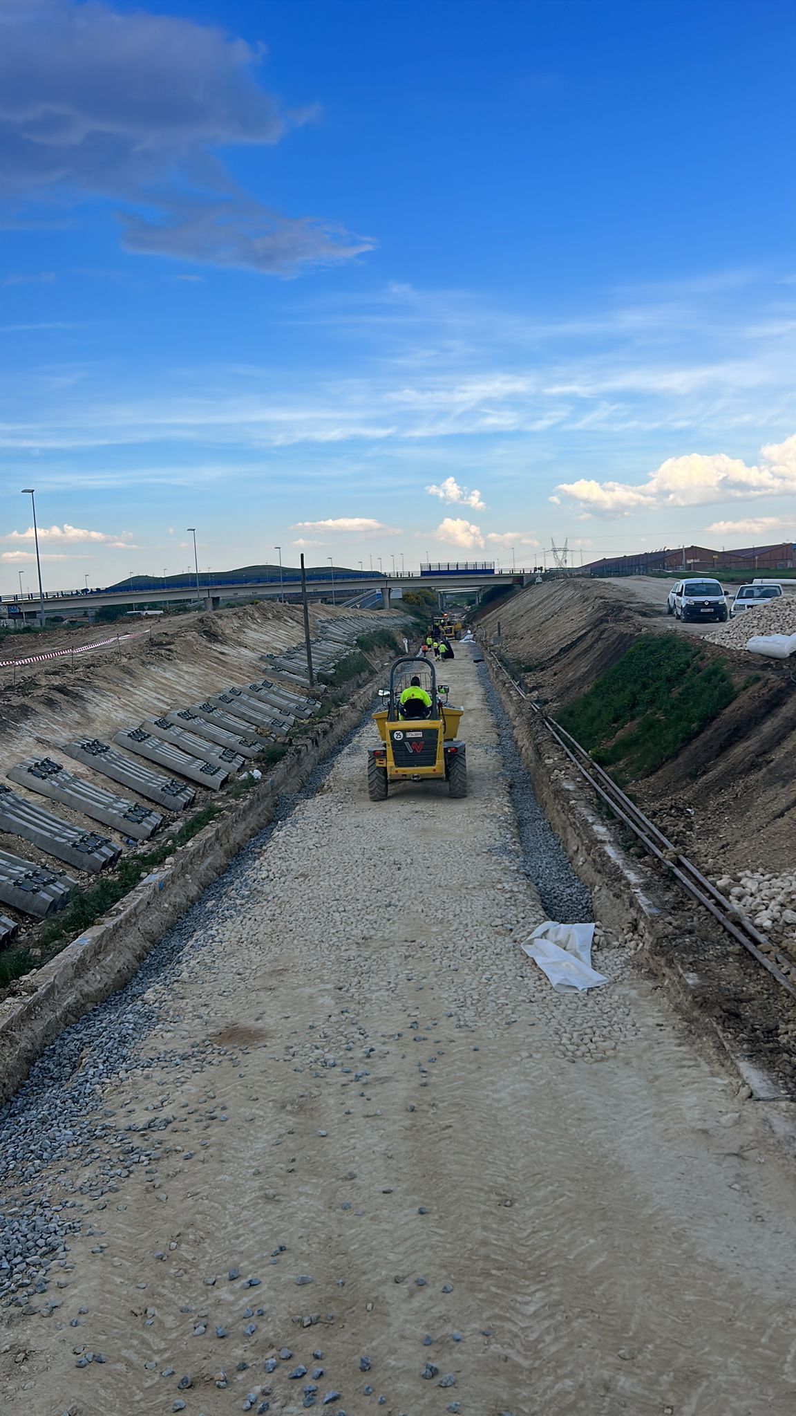 Maquinaria de construcción nivelando una amplia zanja de tierra bajo un cielo azul en una obra de infraestructura.