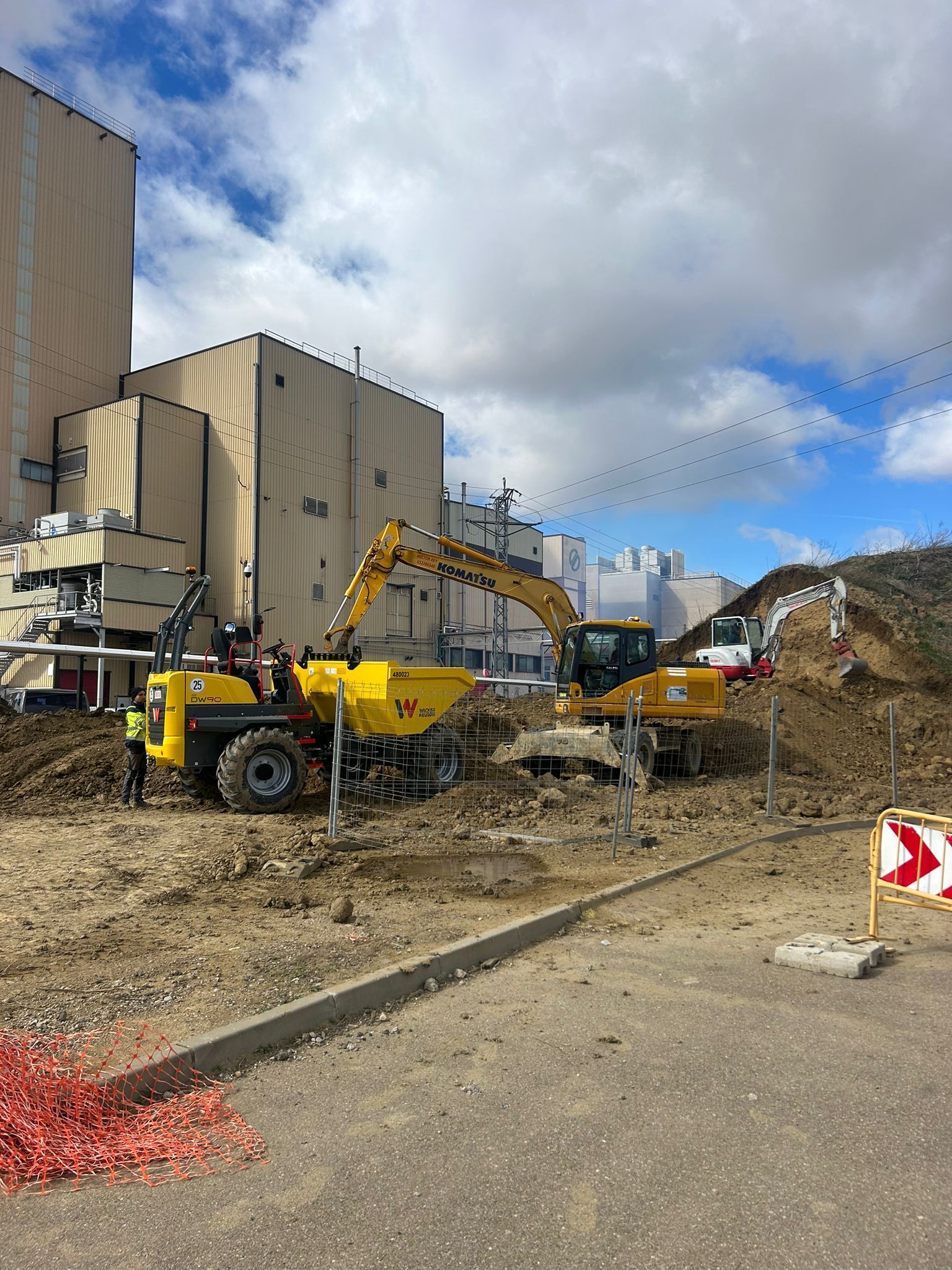 Obra en construcción con excavadoras y maquinaria amarillas junto a un edificio bajo un cielo nublado.