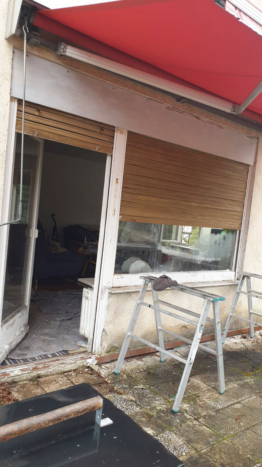 Vor einem Fenster mit roter Markise steht eine Leiter.