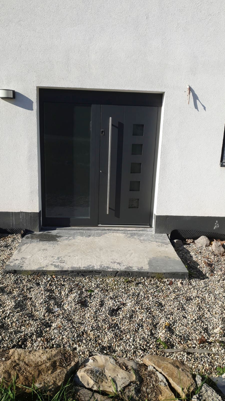 Ein weißes Gebäude mit einer schwarzen Tür und einem Betonweg.