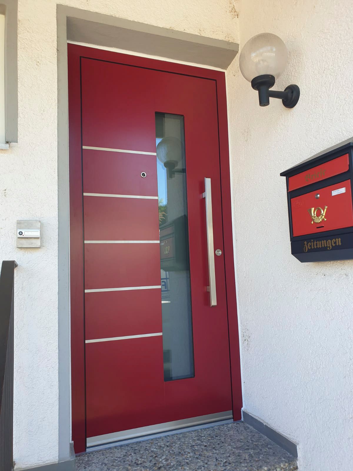 Eine rote Tür an einer weißen Wand neben einem Briefkasten