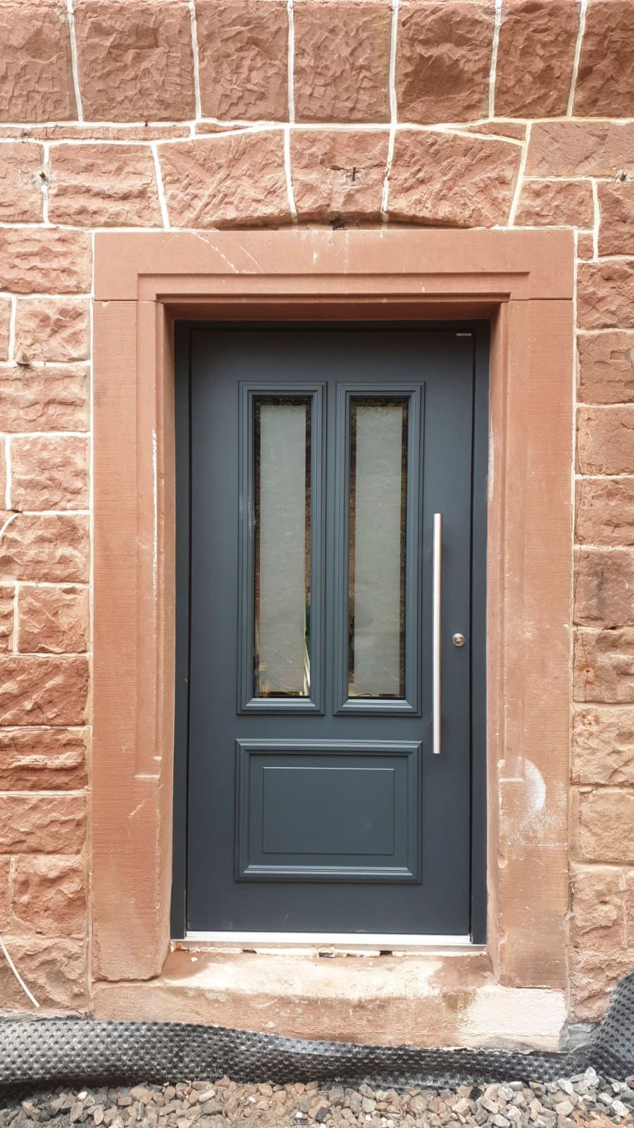 Vor einer Backsteinmauer steht eine schwarze Tür.