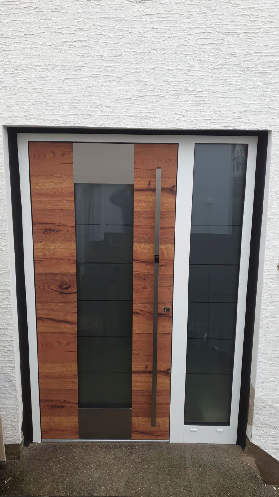 An einem weißen Gebäude befindet sich eine Holztür mit einem Edelstahlgriff.