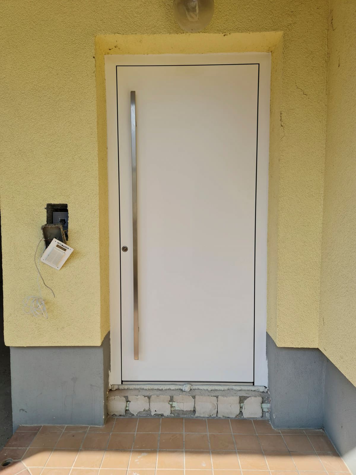 An einer gelben Wand hängt eine weiße Tür mit einem Edelstahlgriff.