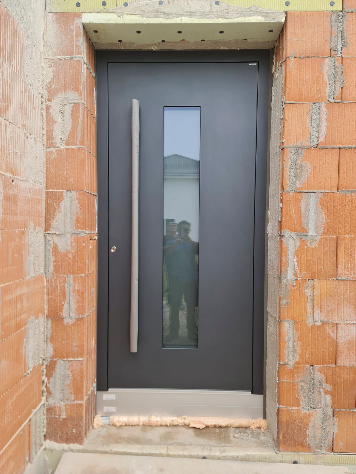 Eine schwarze Tür mit einem Edelstahlgriff befindet sich in einem Backsteingebäude.