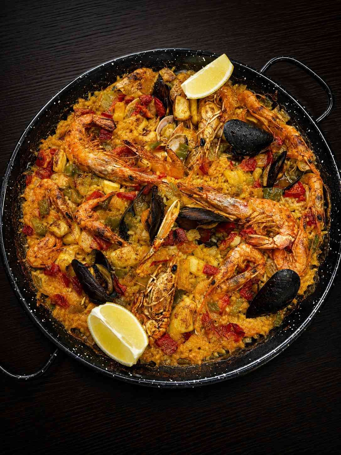 Una paella de marisco con gambas, mejillones y rodajas de limón sobre una mesa oscura.