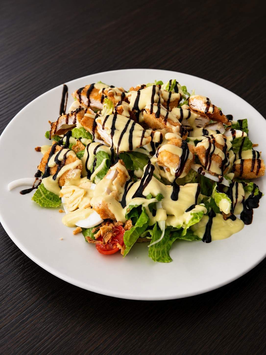 Plato de ensalada con verduras, tomates, pollo a la parrilla y salsa cremosa y oscura.