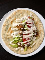 Wrap de pan plano con verduras en rodajas, carne y salsa blanca en un plato blanco.