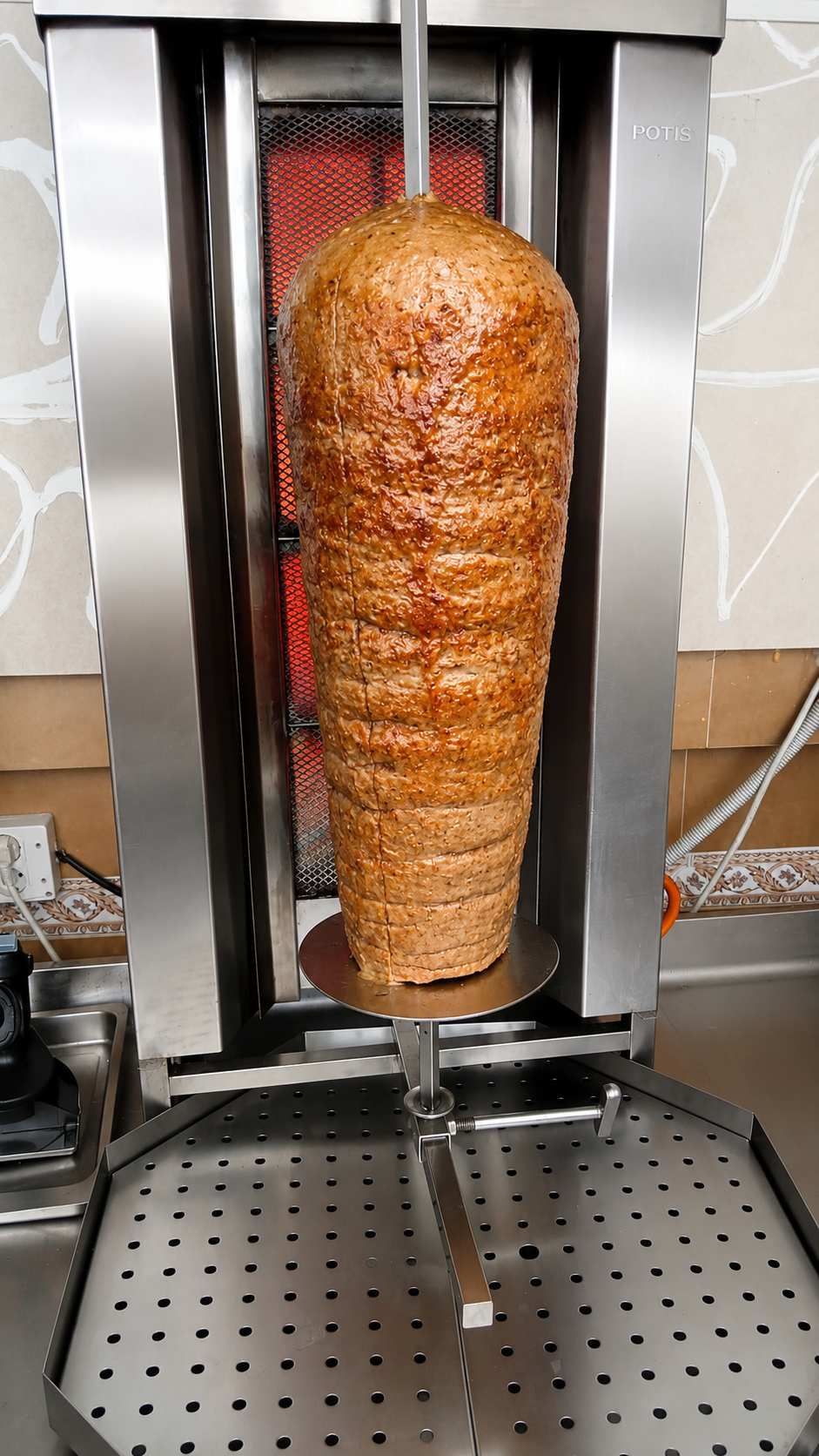 Asador vertical con carne sazonada apilada cocinándose en un asador sobre fuego