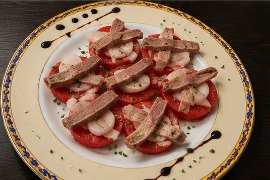 Plato de rodajas de tomate cubiertas con champiñones y salsa roja, adornado con un chorrito de vinagre balsámico.