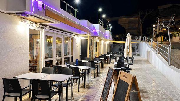 Terraza de café al aire libre por la noche con mesas y sillas vacías, luces cálidas y un sendero nevado.