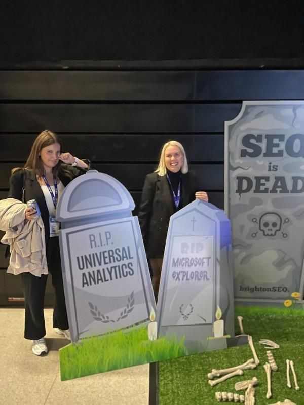 Kaksi naista poseeraa halloween-hautakivirekvisiitta kädessään ja lukee tekstit ”RIP Universal Analytics” ja ”RIP Migrated/Explored”