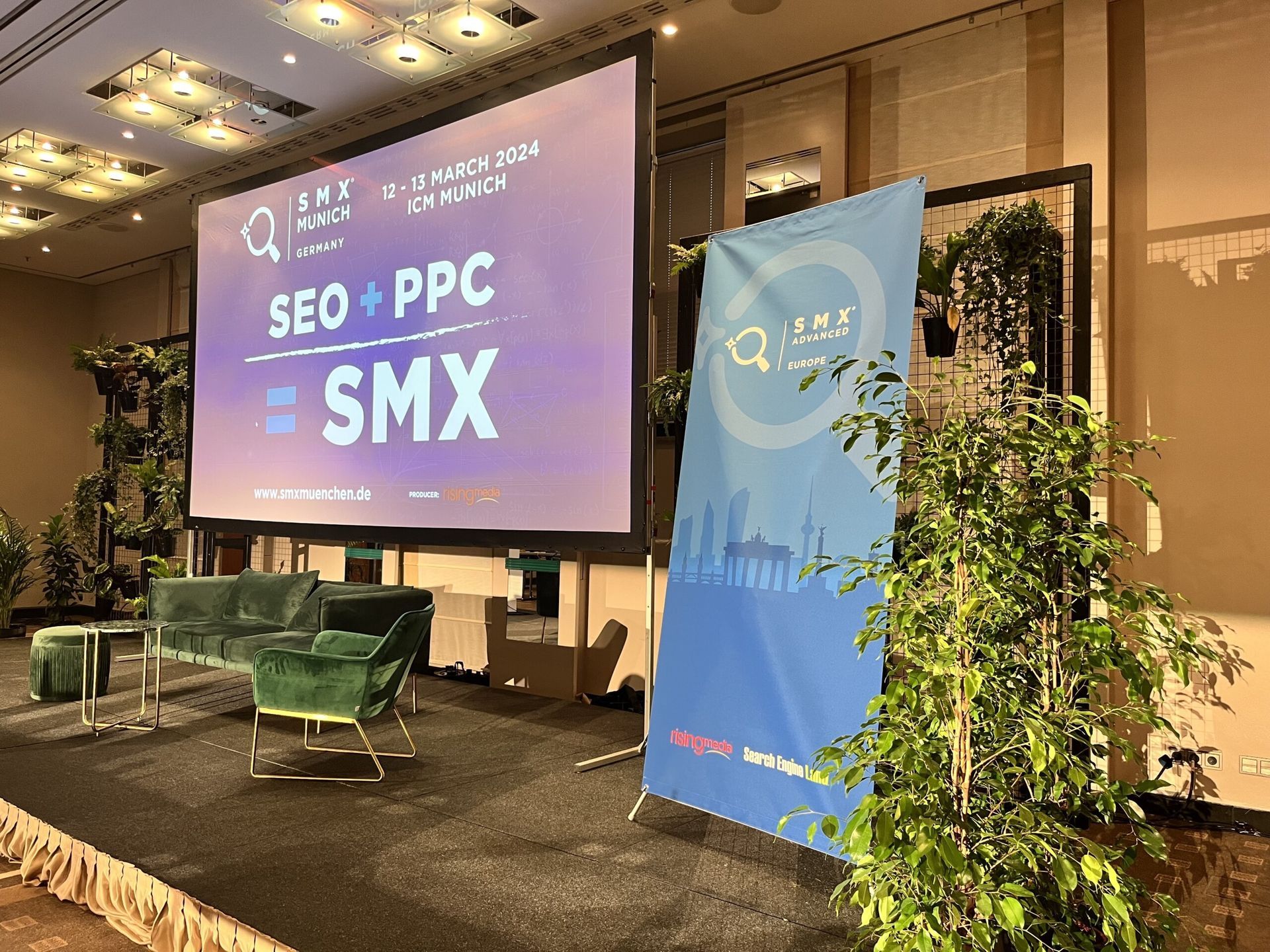 Konferenssilava, jossa on suuri ”SEO + PPC SMX” -näyttö, sininen banneri ja vihreät tuolit juhlasalissa.