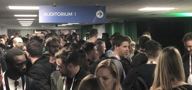 Täysi sisäkäytävä, jossa ihmisiä on kerääntynyt ”Auditorium 1” -kyltin alle