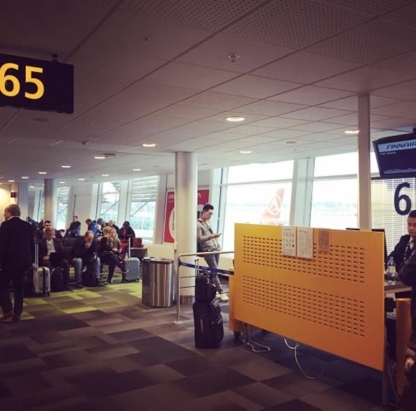 Lentokentän odotusalue, jossa matkustajat istuvat portin 65 lähellä, kirkkaat ikkunat ja oranssit istuinseinät