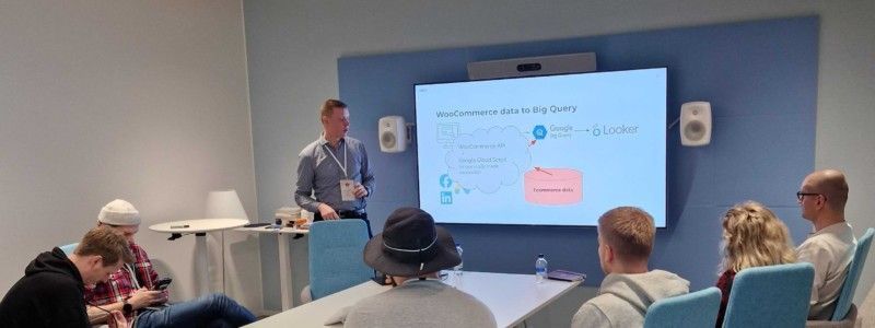 Esittäjä puhuu valkokankaan vieressä kokoushuoneessa, yleisön istuessa kuuntelemassa.