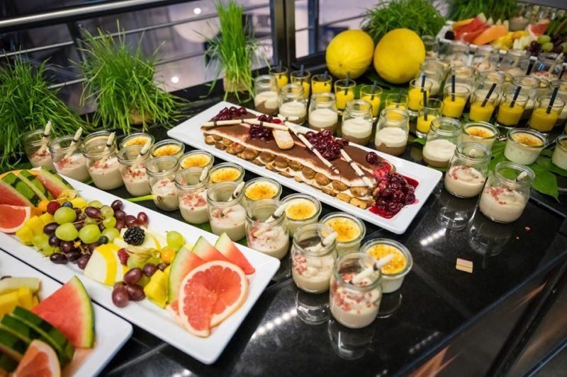 Elegantti buffetpöytä, jossa on hedelmiä, jälkiruokia ja pieniä alkupalakuppeja mustalla työtasolla