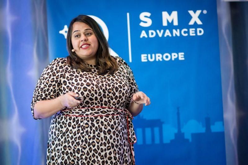 Puhuja lavalla SMX Advanced Europessa, yllään leopardikuvioinen mekko, takanaan sininen tapahtumatausta