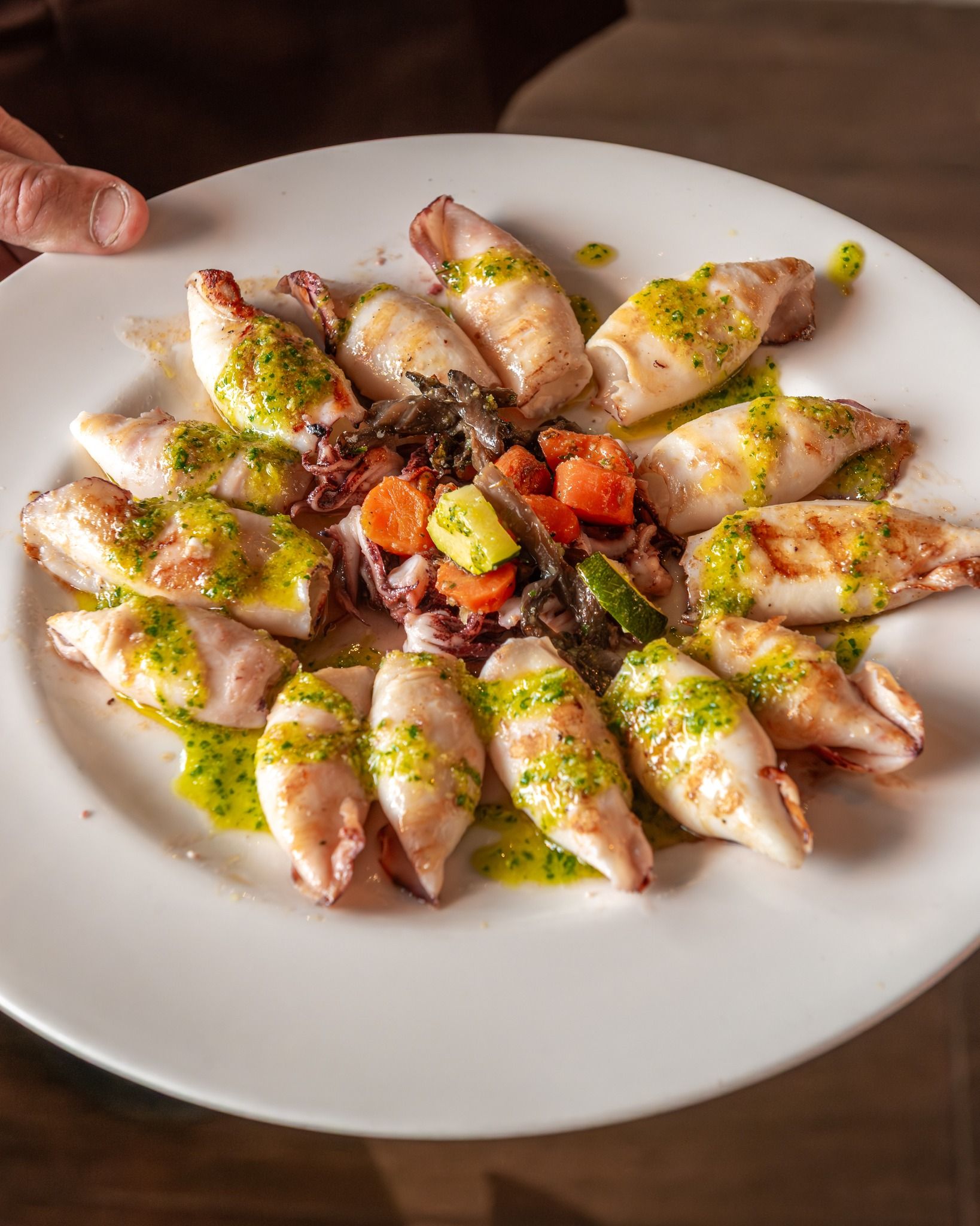 Una persona sostiene un plato de comida con calamares y verduras.