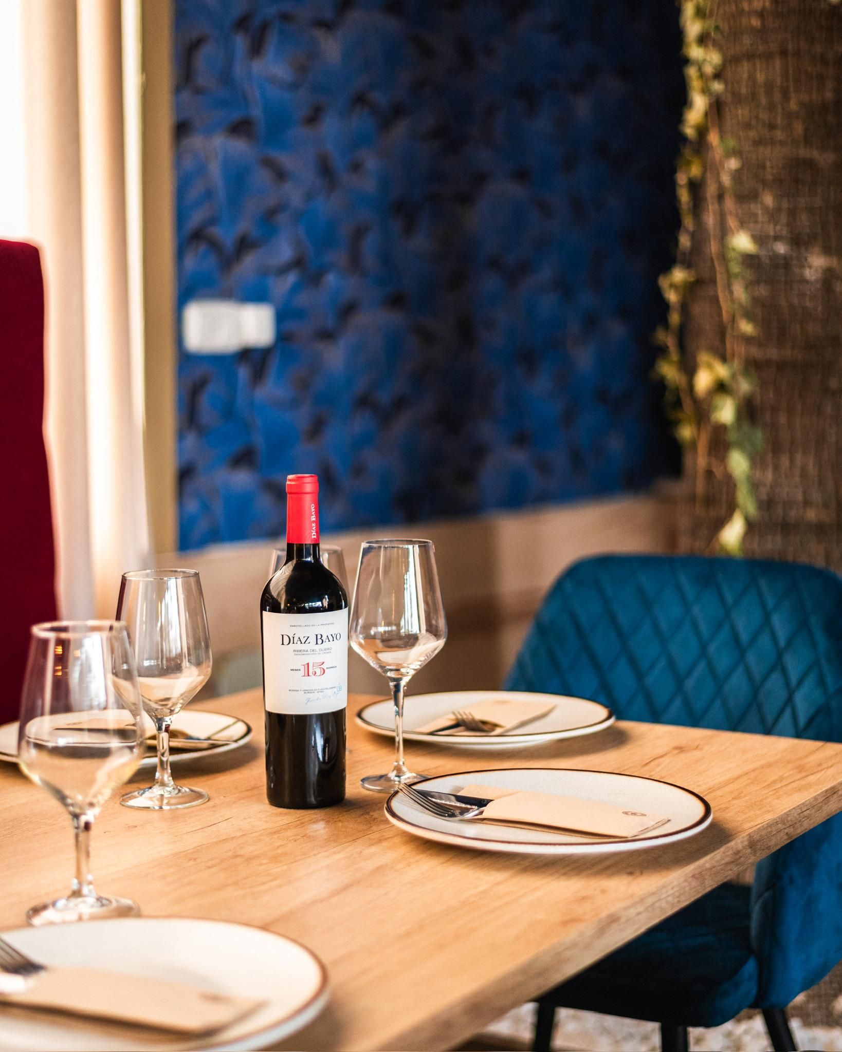 Una botella de vino está sobre una mesa de madera con platos y vasos.