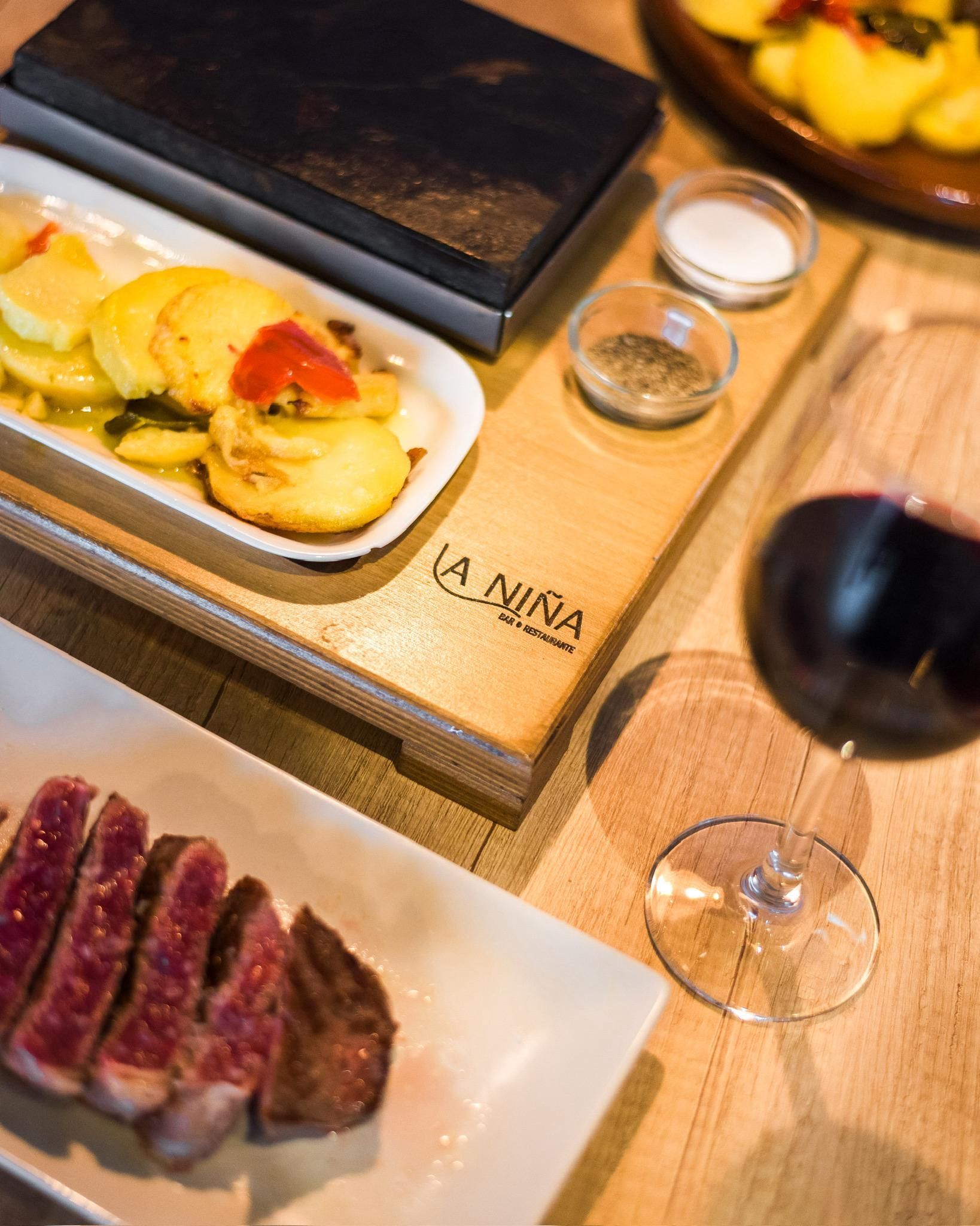 Una mesa de madera con platos de comida y una copa de vino.