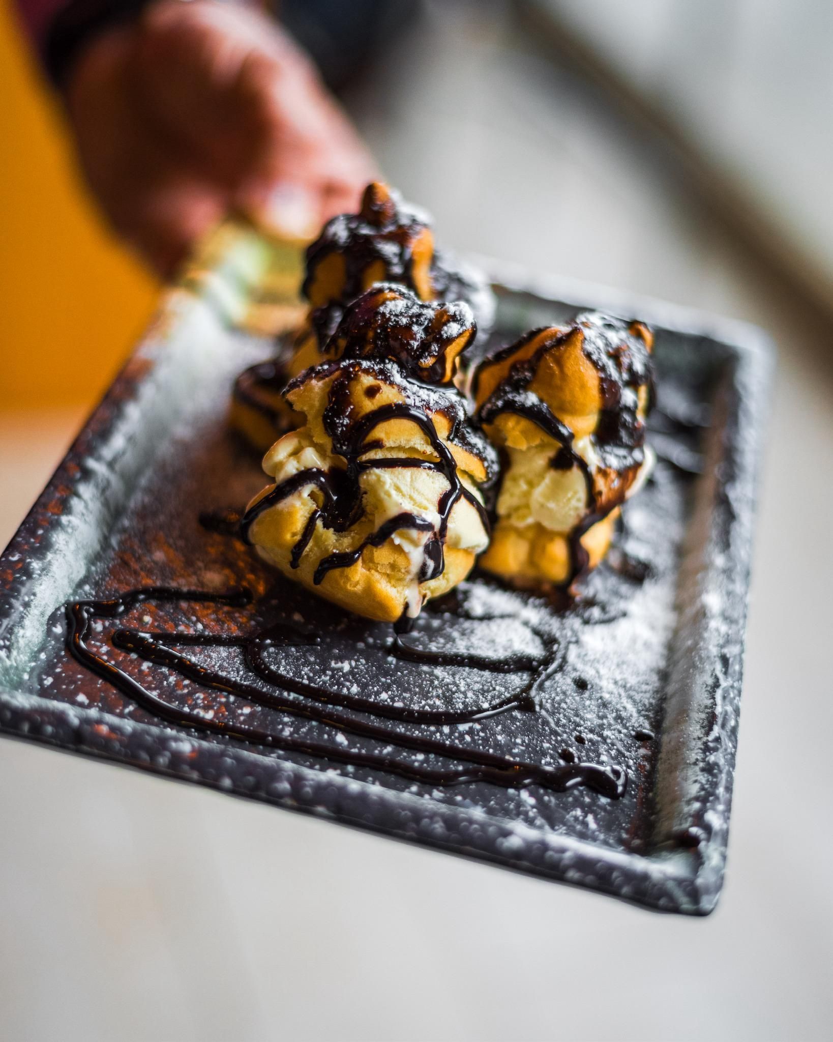 Una persona sostiene un plato de postre con salsa de chocolate y azúcar en polvo.