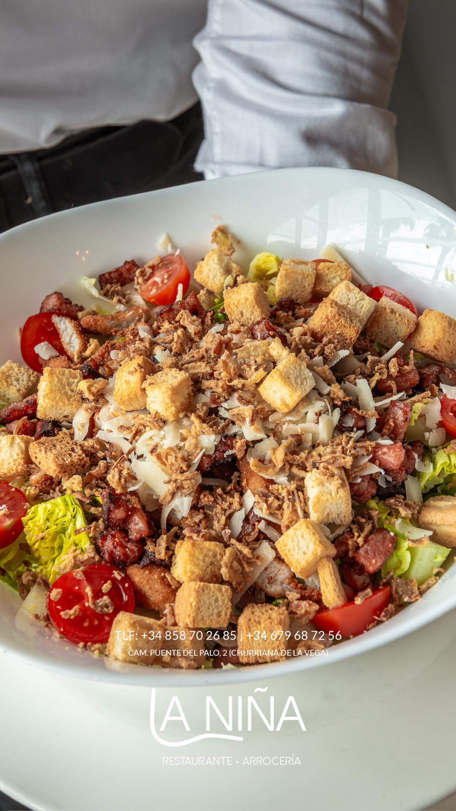 Una persona sostiene un tazón de ensalada con crutones y tomates.