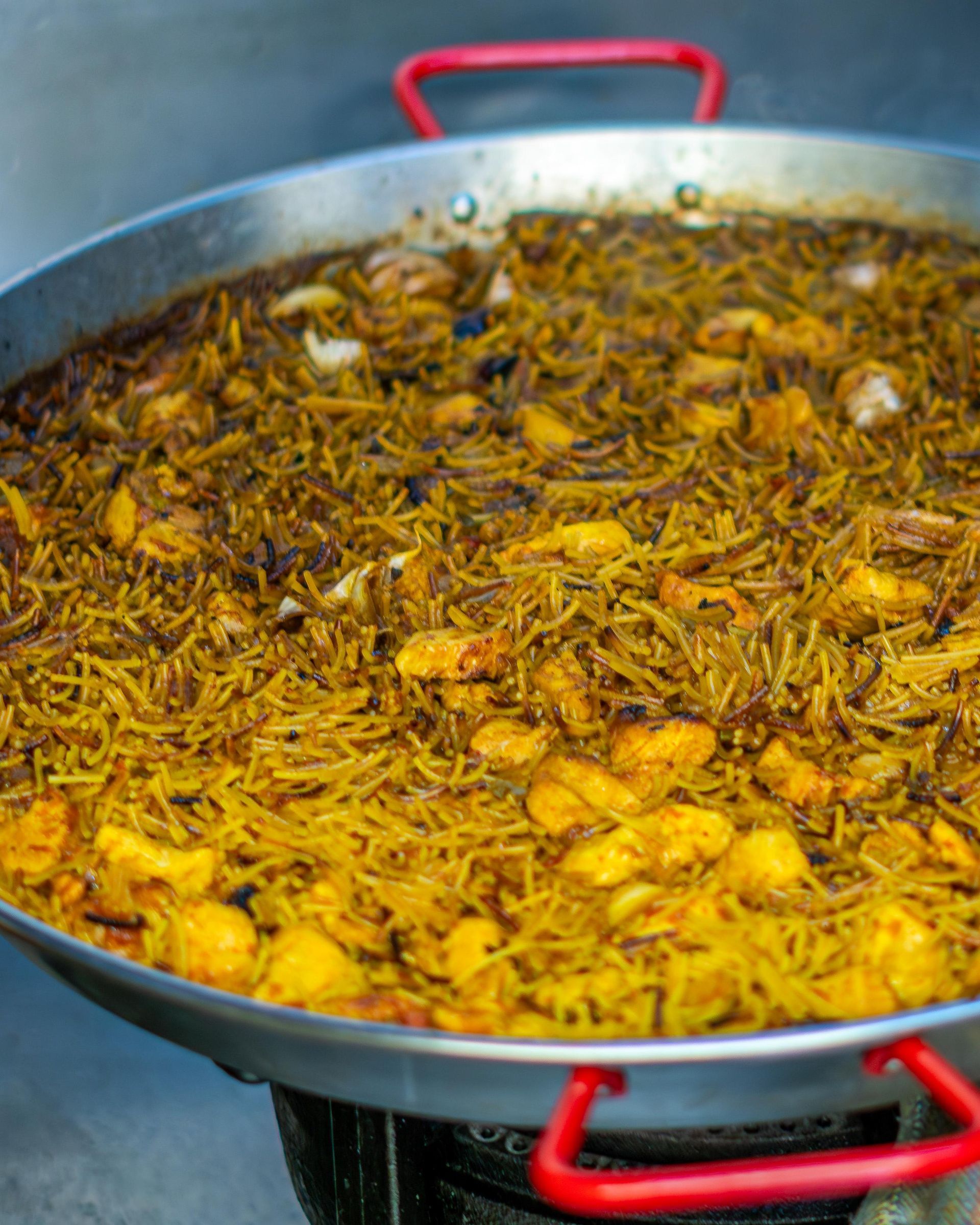Una persona sostiene una sartén de paella con camarones y champiñones.