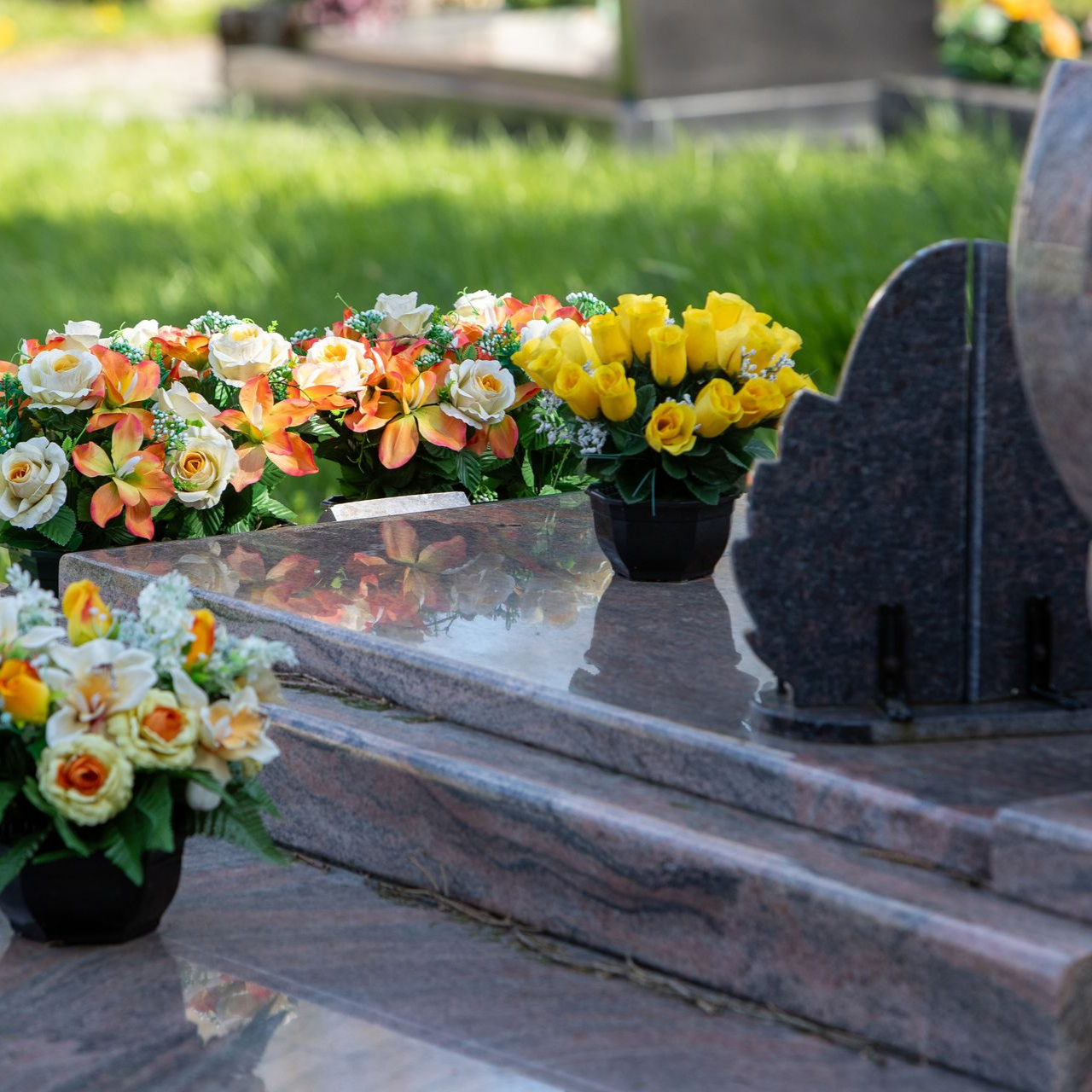 Une pierre tombale en granit poli dans un cimetière, ornée de bouquets de fleurs jaunes, oranges et blanches.