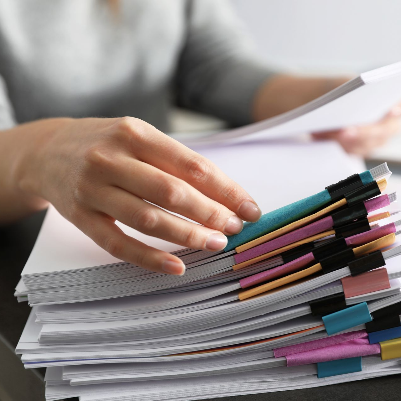 Une personne range une pile de feuilles blanches maintenues par des pinces à reliure colorées.