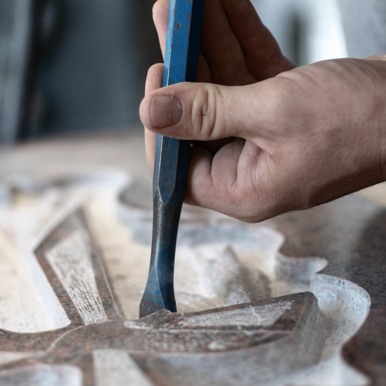 Gros plan sur une main utilisant un ciseau en métal bleu pour sculpter des motifs complexes dans un morceau de pierre polie.