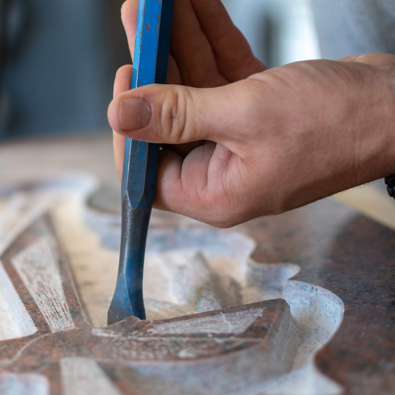Une personne utilise un ciseau en métal bleu pour sculpter un motif détaillé sur une surface de pierre lisse et polie.