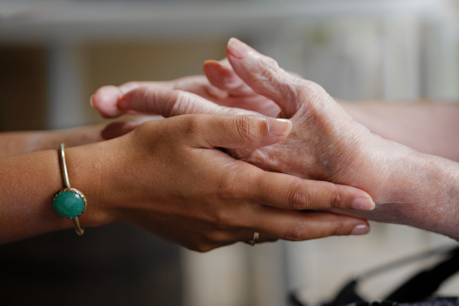 Une personne portant un bracelet en pierre verte tient la main d'une autre personne dans un geste d'attention et de soutien.