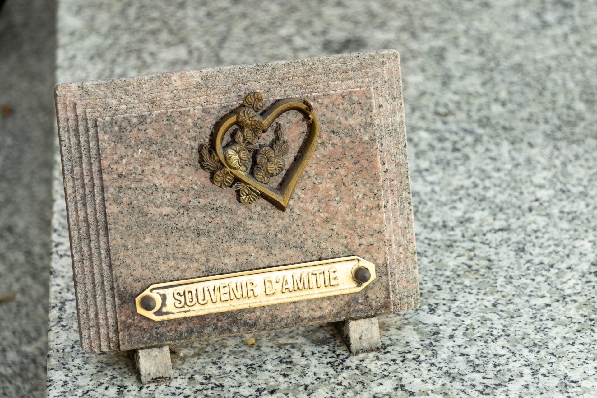 Une petite plaque commémorative en granit avec un emblème de cœur doré et une plaque portant l'inscription SOUVENIR D'AMITIÉ sur une surface en pierre.