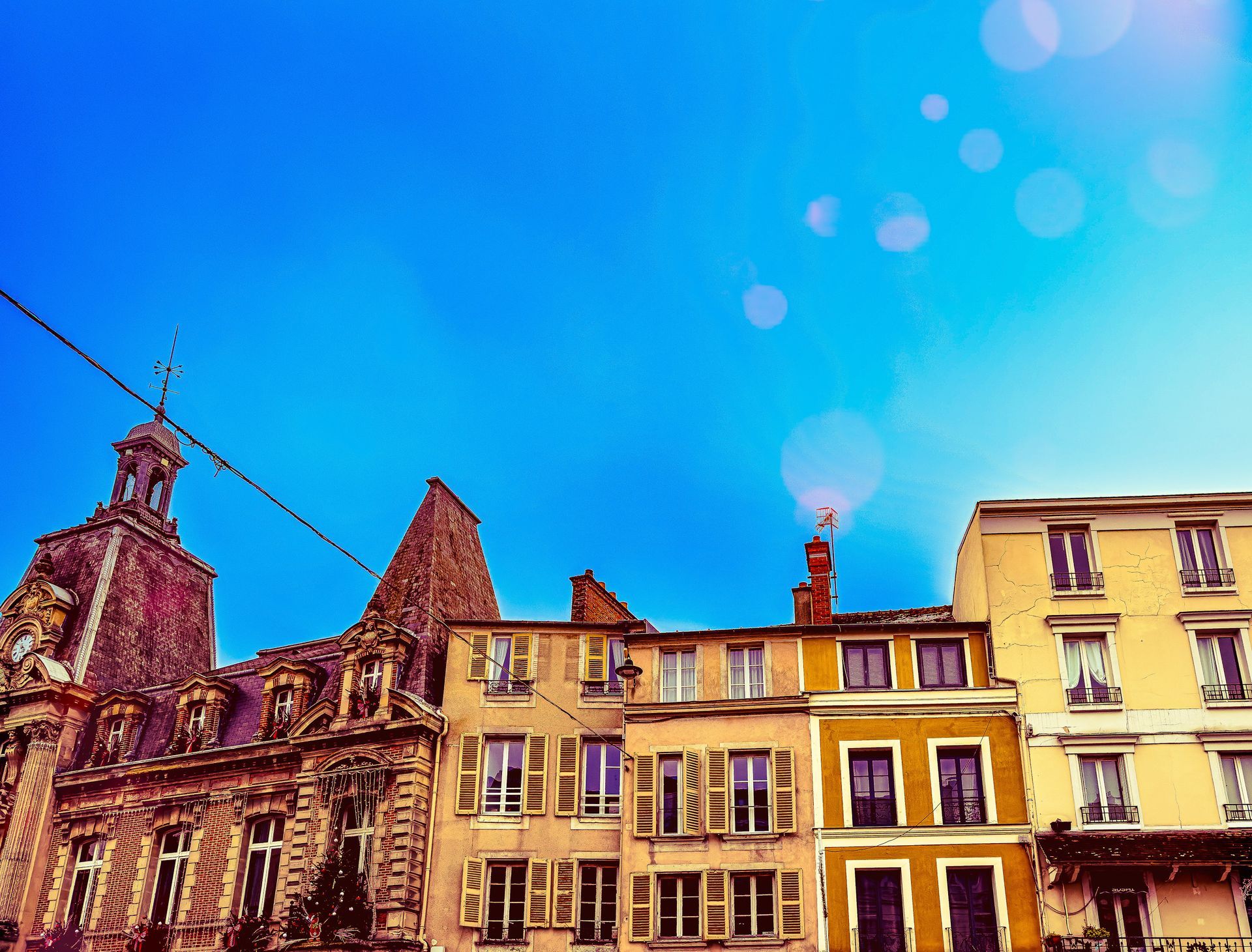 Architecture traditionnelle avec une tour en pierre historique jouxtant des immeubles résidentiels crème et jaune sous un ciel lumineux.