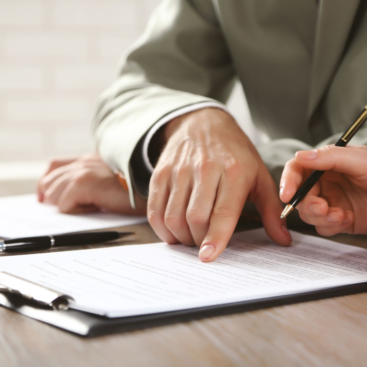 Deux paires de mains examinent et signent un document sur un bloc-notes, signifiant une réunion d'affaires ou un accord contractuel.