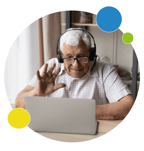 Homme âgé qui regarde un ordinateur portable en faisant un geste de bonjour de la main et portant un casque audio