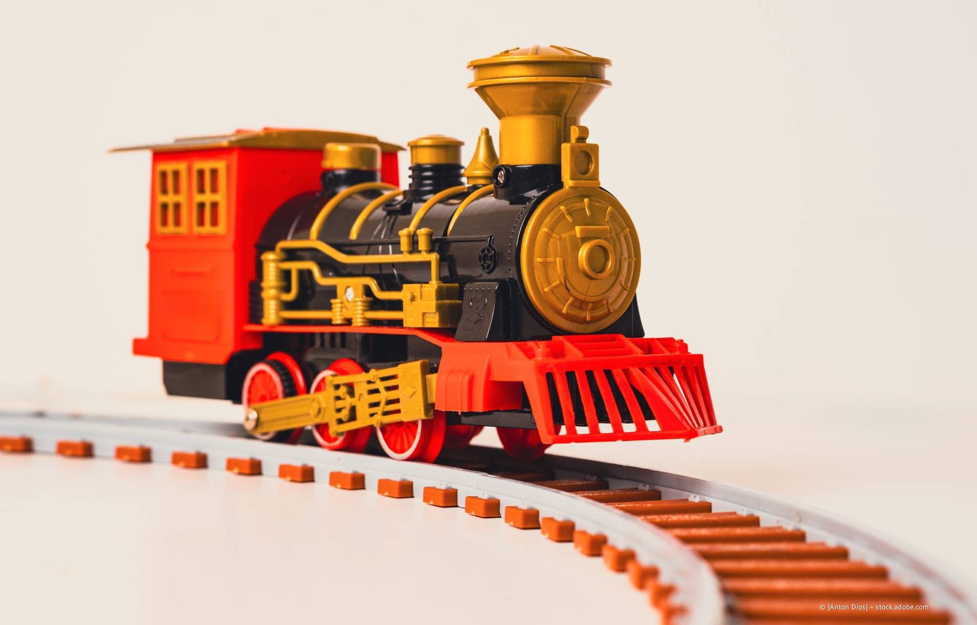 Spielzeugeisenbahn, rot und schwarz, auf gebogenen braunen Gleisen, vor weißem Hintergrund.